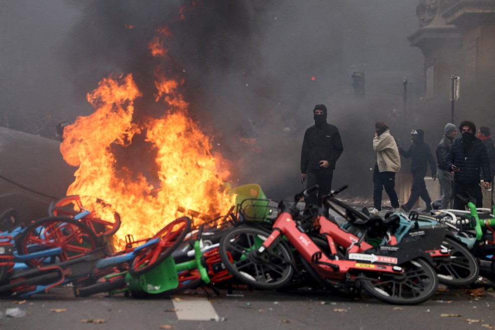 Manifestantes mascarados permanecem ao lado de bicicletas em chamas durante confrontos em uma manifestação contra o custo de vida e a alta dos preços dos combustíveis — Foto: Reuters/Jack Taylor