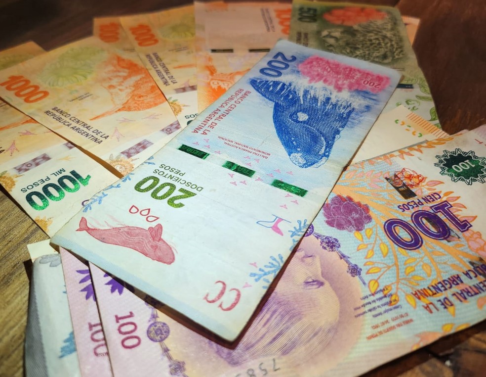 Notas de peso argentino em contagem, indicando a desvalorização da moeda.