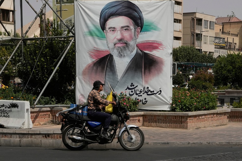 Um homem passa de carro por um cartaz com um retrato do líder supremo do Irã, aiatolá Mojtaba Khamenei, no centro de Teerã, no Irã, na segunda-feira, 31 de agosto de 2026 — Foto: AP/Vahid Salemi