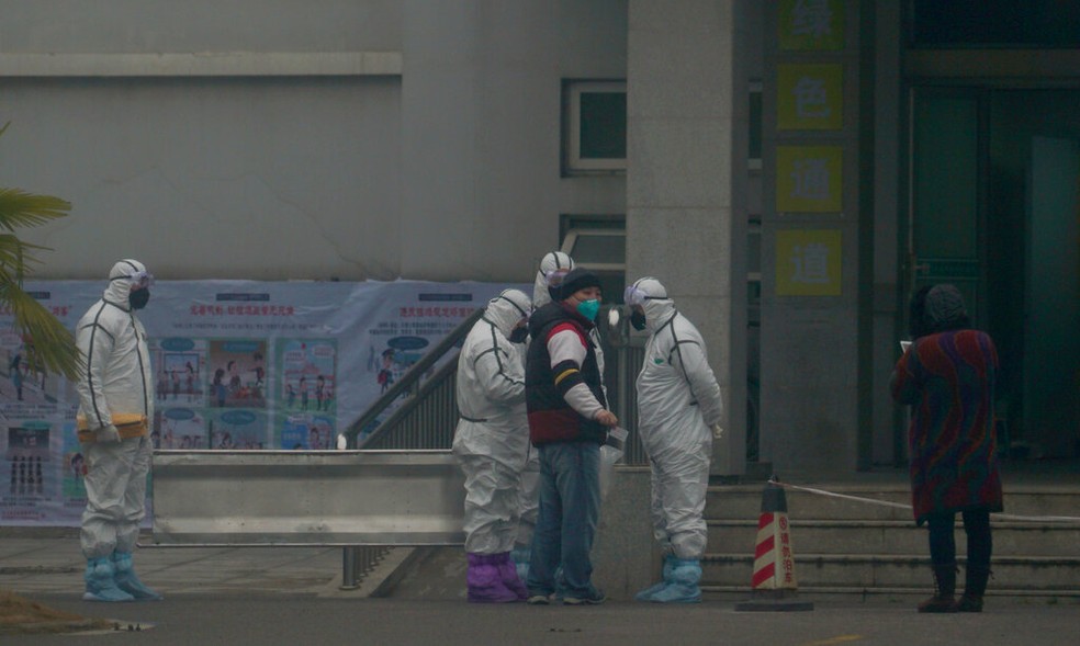 Funcionários em trajes de risco biológico à frente do pronto-socorro do Centro de Tratamento Médico de Wuhan — Foto: Dake Kang/AP
