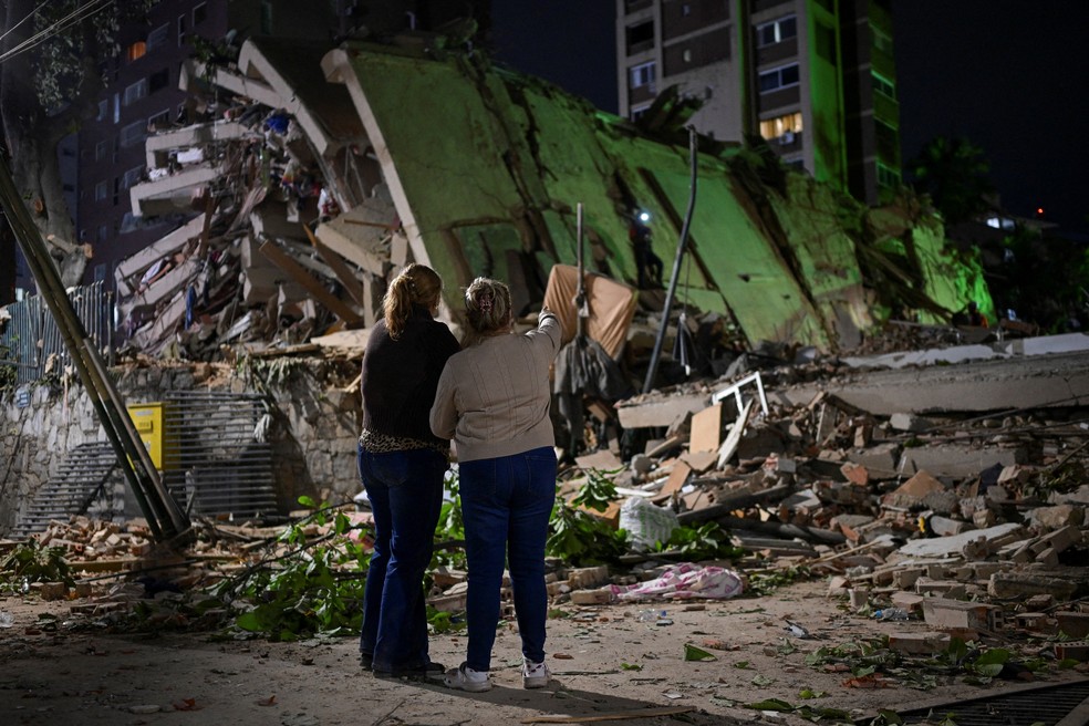Fanny Nasri aguarda no local de um prédio que desabou enquanto equipes de emergência procuram por seu filho, Antonio Nasri, ao lado de Noemi Cordoba, que aguarda notícias de sua neta, após um terremoto em Caracas, Venezuela , em 25 de junho de 2026 — Foto: REUTERS/Gaby Oraa