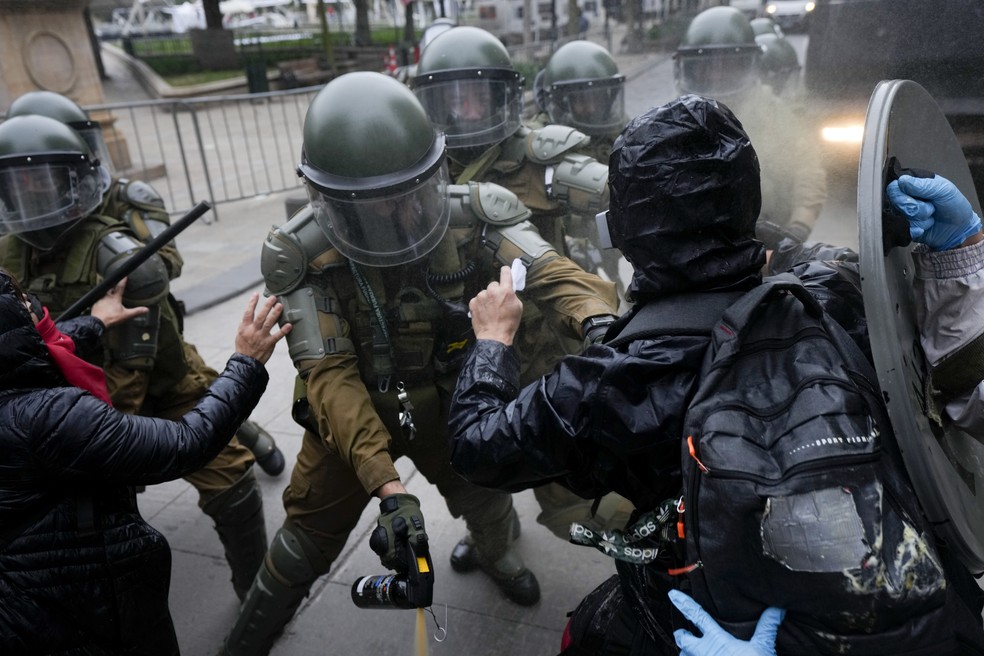 Grupos de encapuzados em confronto com a polícia durante marcha contra a ditadura no Chile — Foto: Esteban Félix/AP