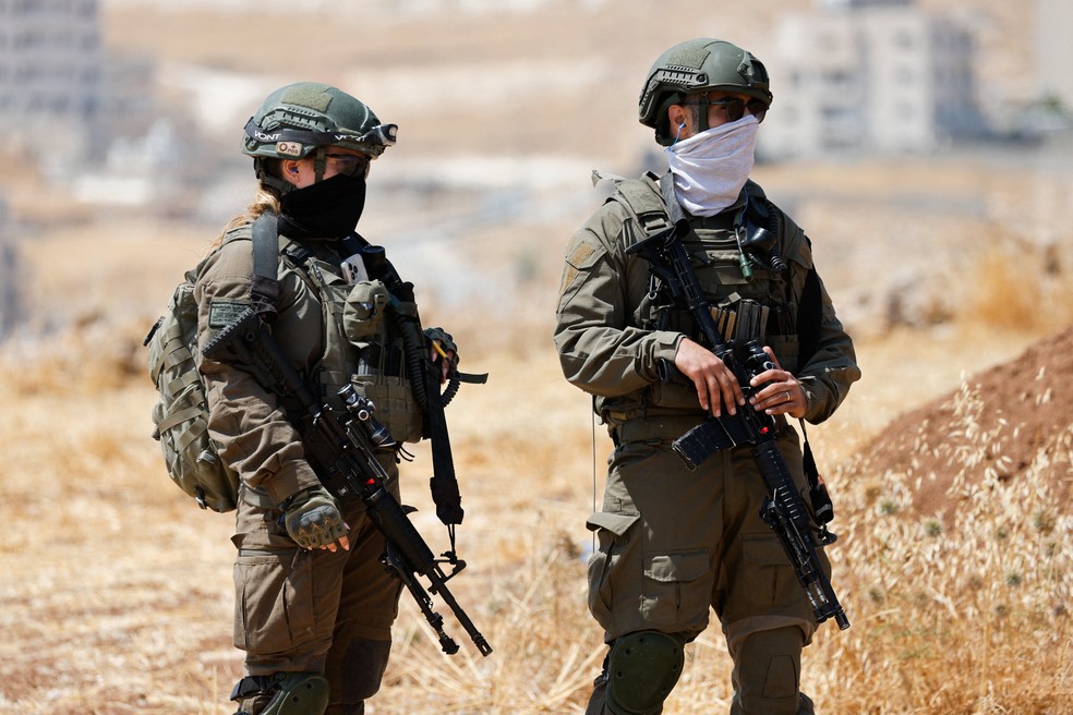 Soldados israelenses observam enquanto ativistas palestinos e israelenses acompanham proprietários palestinos em sua propriedade, ameaçada de confisco por colonos israelenses, em Beit Sahour, na Cisjordânia ocupada por Israel, em 14 de agosto de 2026 — Foto: REUTERS/Mussa Qawasma