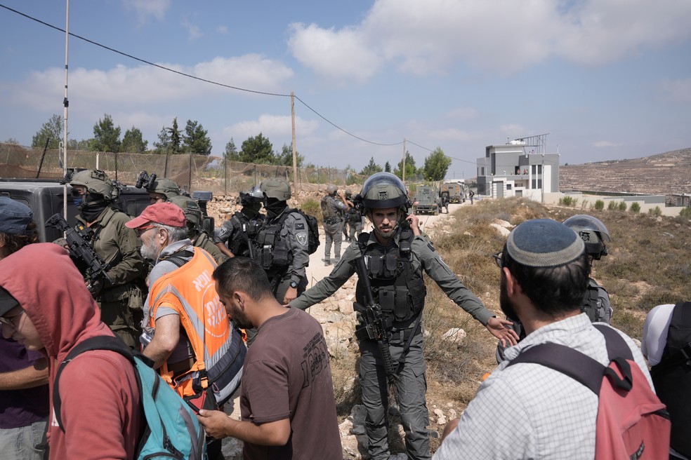 Soldados do Exército israelense impedem o avanço de ativistas que marchavam com alimentos e água em direção às casas de três famílias palestinas sitiadas por colonos israelenses há seis dias, na vila de Qusra, na Cisjordânia ocupada, ao sul de Nablus, em 14 de agosto de 2026 — Foto: AP Photo/Majdi Mohammed