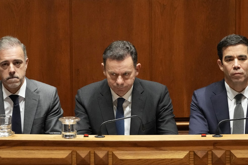O primeiro-ministro de Portugal, Luis Montenegro, ladeado pelo ministro dos Assuntos Parlamentares, Pedro Duarte, à esquerda, e pelo ministro do Gabinete, António Leitão Amaro, reagem após a moção de confiança do governo ter sido rejeitada em uma votação no Parlamento português, em Lisboa, terça-feira, 11 de março de 2025 — Foto: Armando Franca/AP