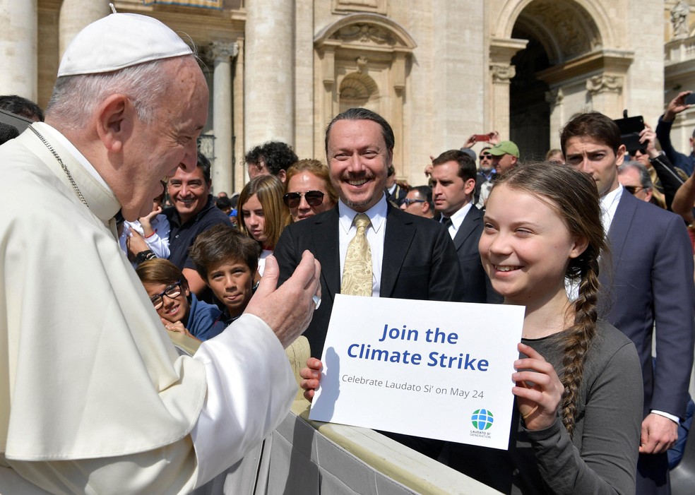 Papa Francisco cumprimenta a ativista climática Greta Thunberg, que carrega um cartaz com referência ao “Laudato Si” — Foto: Abaca Press/Sipa USA via AP