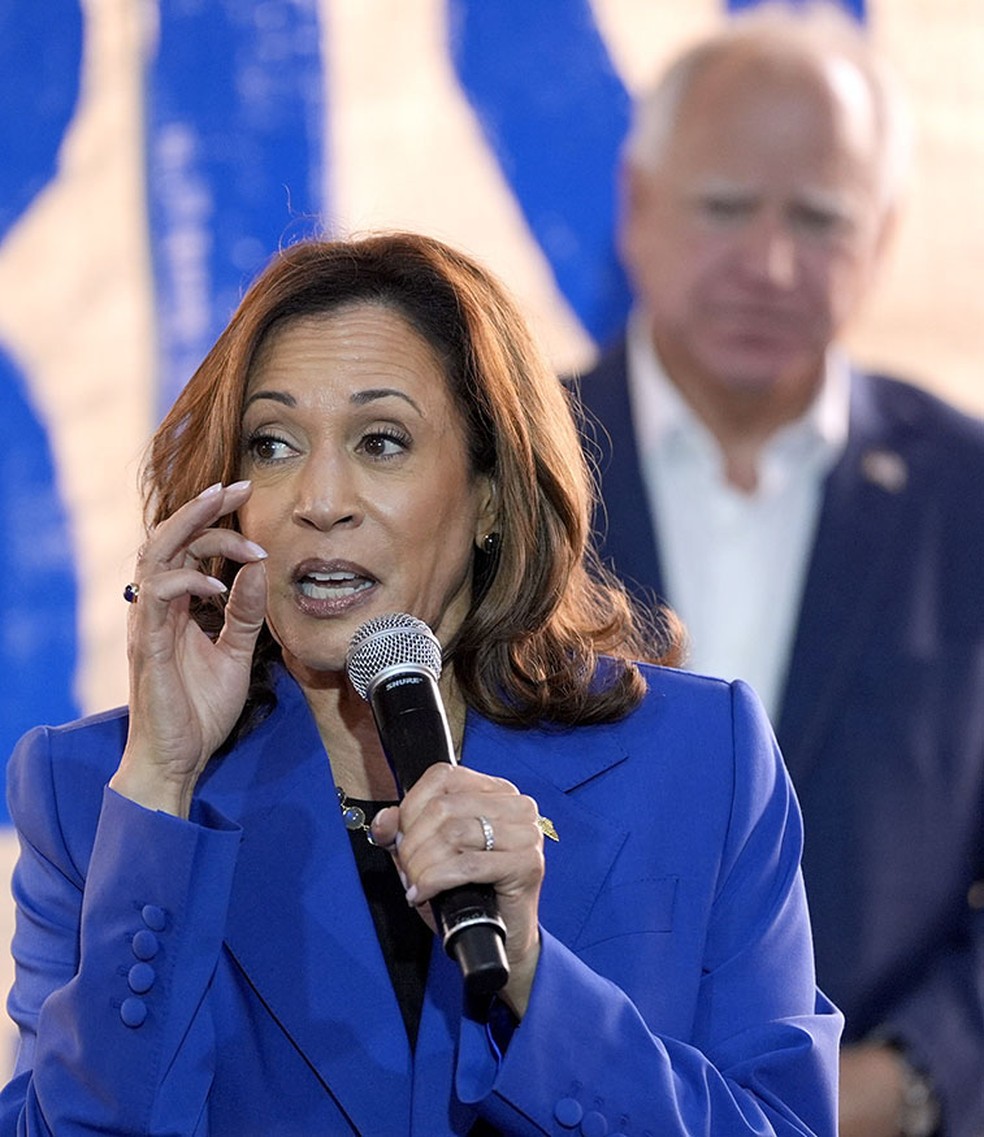 Kamala Harris, com seu candidato a vice Tim Walz ao fundo, em campanha — Foto: AP Photo/Julia Nikhinson