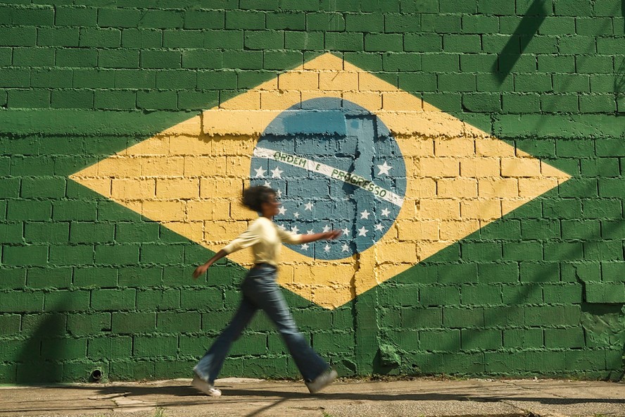 Mulher caminha com bandeira do Brasil ao fundo