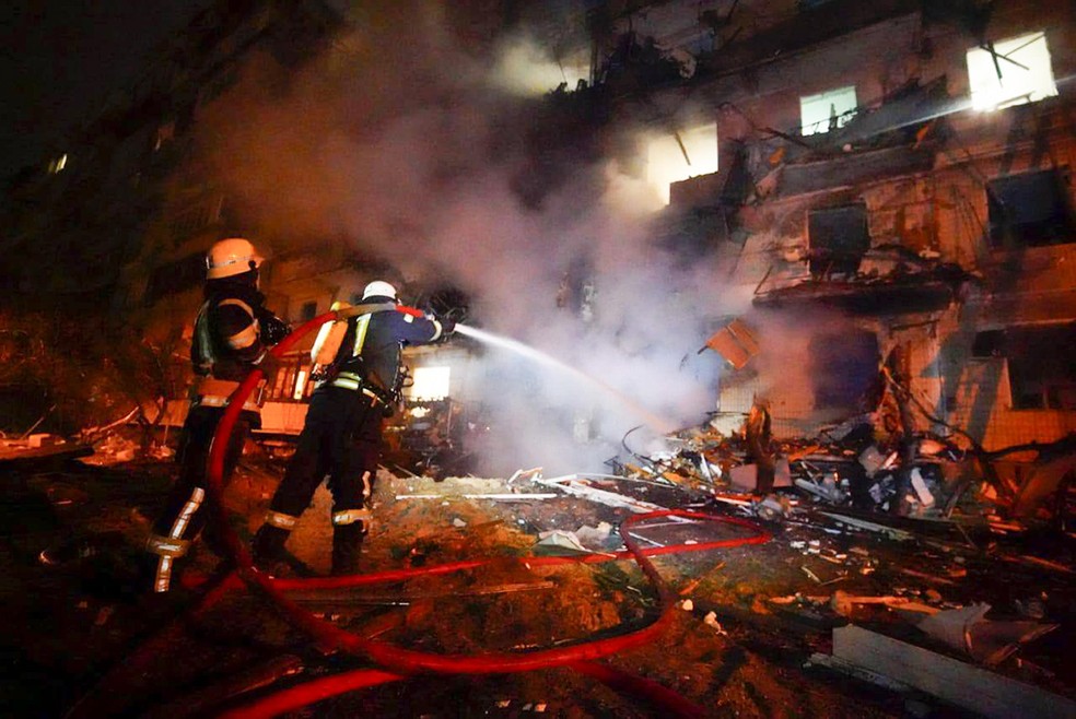 Nesta foto tirada de um vídeo, os bombeiros atuam sobre destroços em chamas em frente a um prédio danificado — Foto: Reprodução via AP