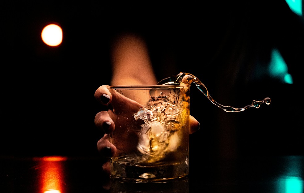 Homem bebe em um copo com gelo em um bar.